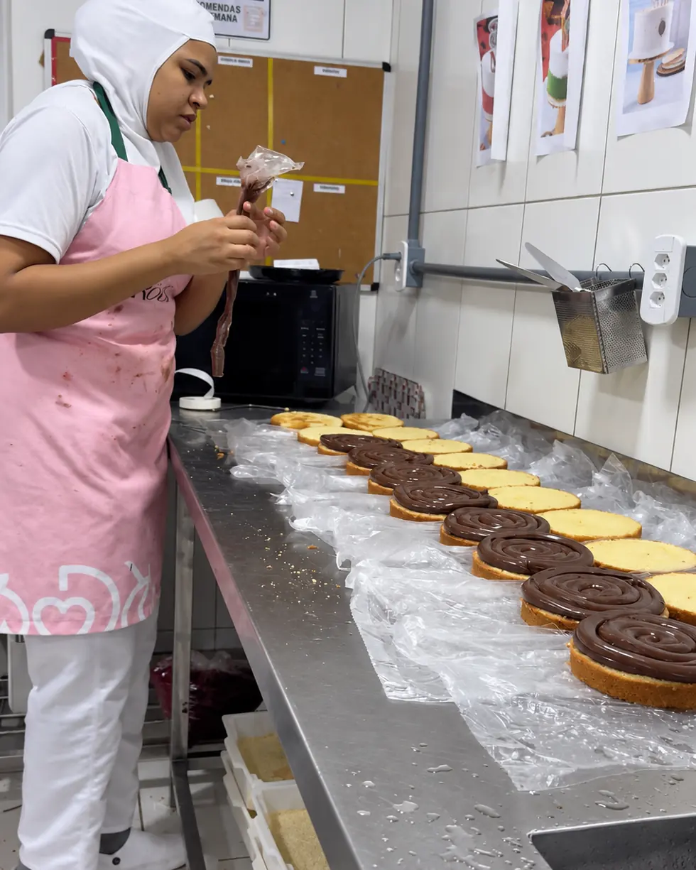 Colaboradora da Rôof anotando a etiqueta na bancada, com tortas montadas enfileiradas ao lado