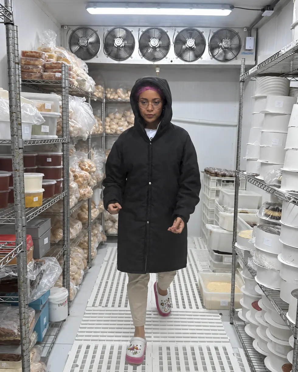 Rôof França caminhando dentro da câmara fria da confeitaria, entre prateleiras de produtos organizados
