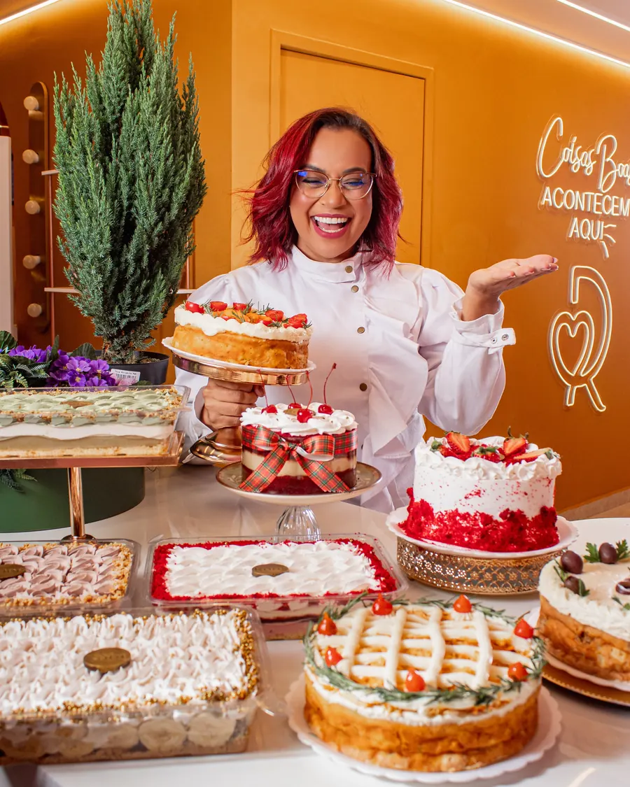Rôof França de dólmã branca, sorrindo, cercada por bolos e tortas decorados na loja da Rôof